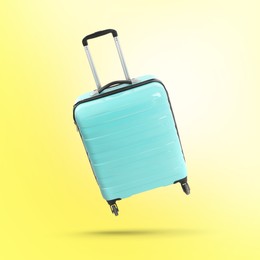 Image of Turquoise suitcase in air on yellow background