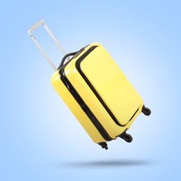 Yellow suitcase in air on light blue background