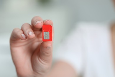 Woman holding SIM card indoors, closeup. Space for text