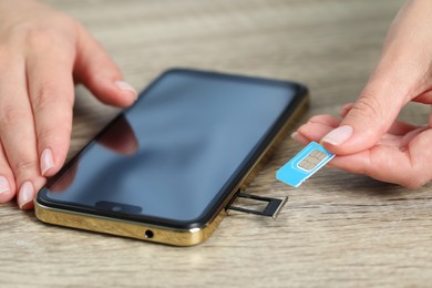 Photo of Woman holding SIM card near smartphone at wooden table, closeup