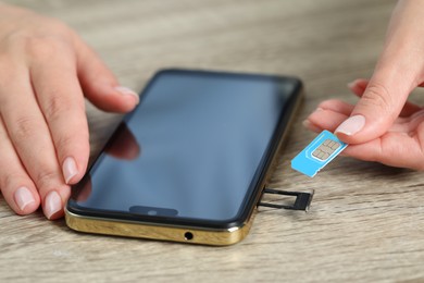 Woman holding SIM card near smartphone at wooden table, closeup