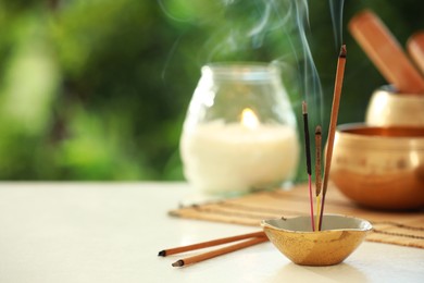 Photo of Incense sticks smoldering in holder, Tibetan singing bowl and candle on light table outdoors, space for text