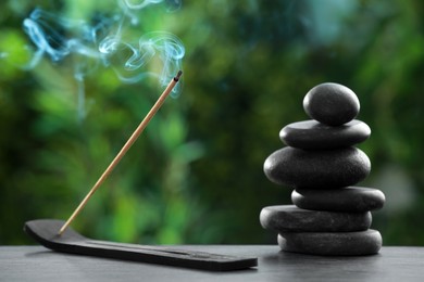 Photo of Incense stick smoldering in holder and spa stones on wooden table outdoors