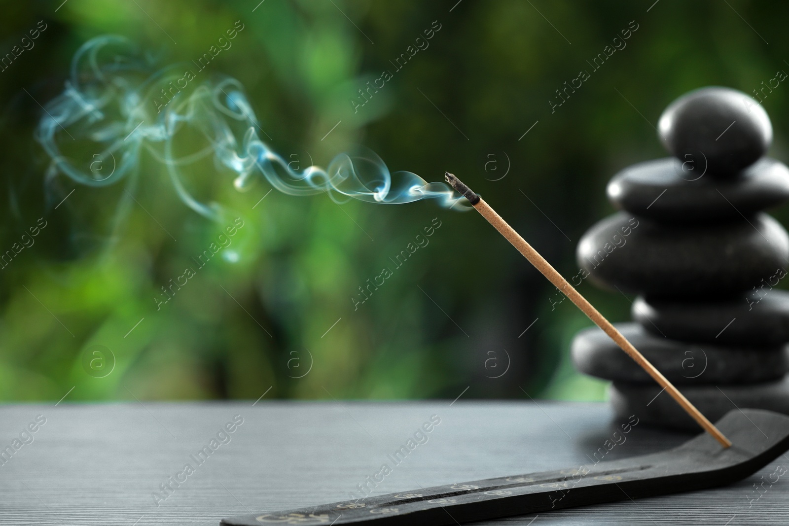 Photo of Incense stick smoldering in holder and spa stones on wooden table outdoors. Om ligature