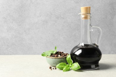 Photo of Balsamic vinegar in glass jug, herbs and spices on gray textured table, space for text