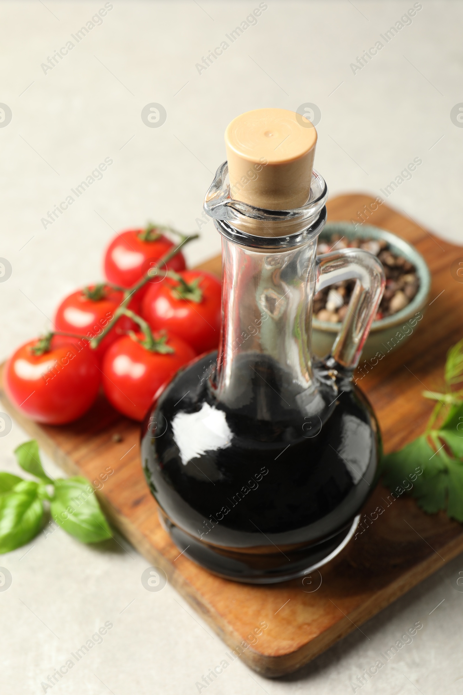 Photo of Balsamic vinegar in glass jug, tomatoes, herbs and spices on gray textured table, closeup