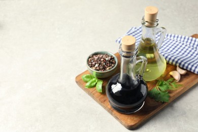 Photo of Balsamic vinegar in glass jug, oil, herbs and spices on gray textured table, space for text