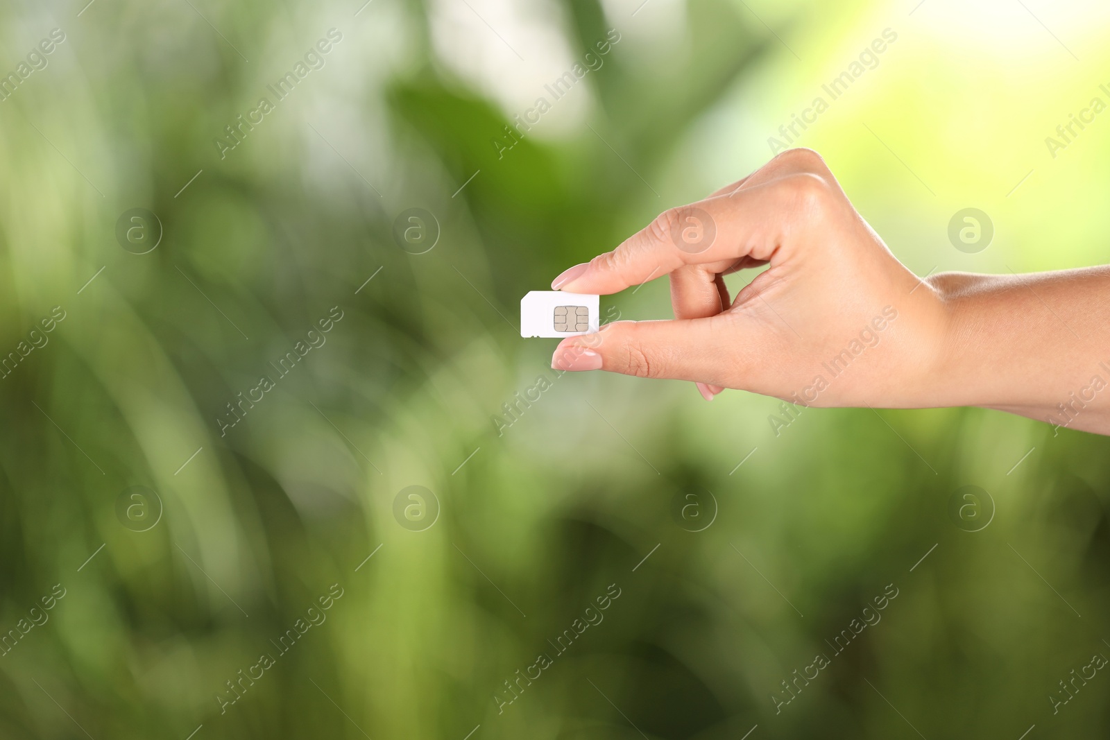 Photo of Woman holding SIM card on blurred background, closeup. Space for text