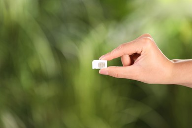 Photo of Woman holding SIM card on blurred background, closeup. Space for text