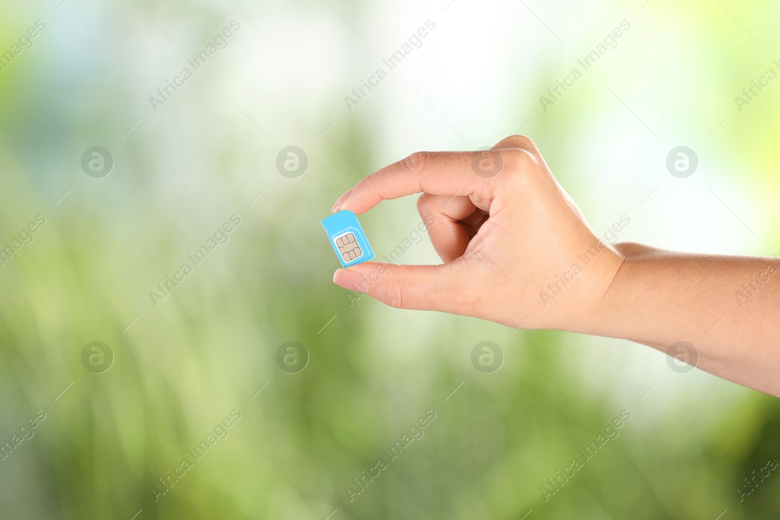 Photo of Woman holding SIM card on blurred background, closeup. Space for text