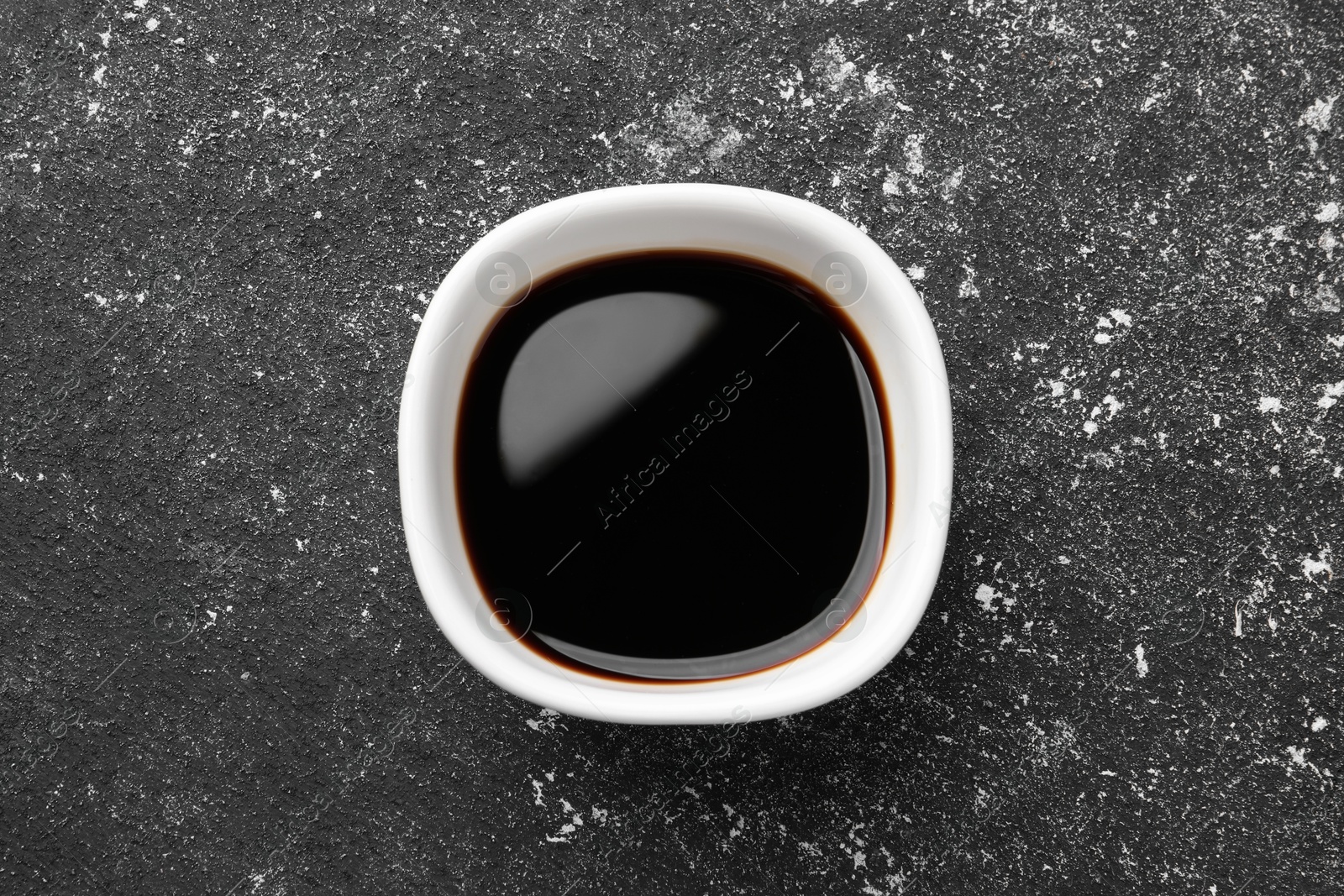 Photo of Balsamic vinegar in bowl on black textured table, top view