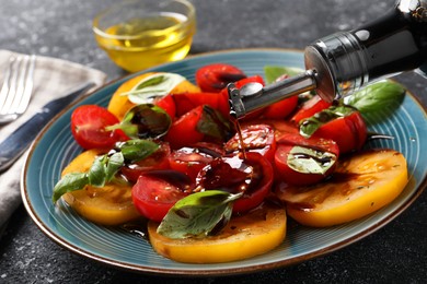 Photo of Pouring balsamic vinegar onto tasty salad on black textured table, closeup