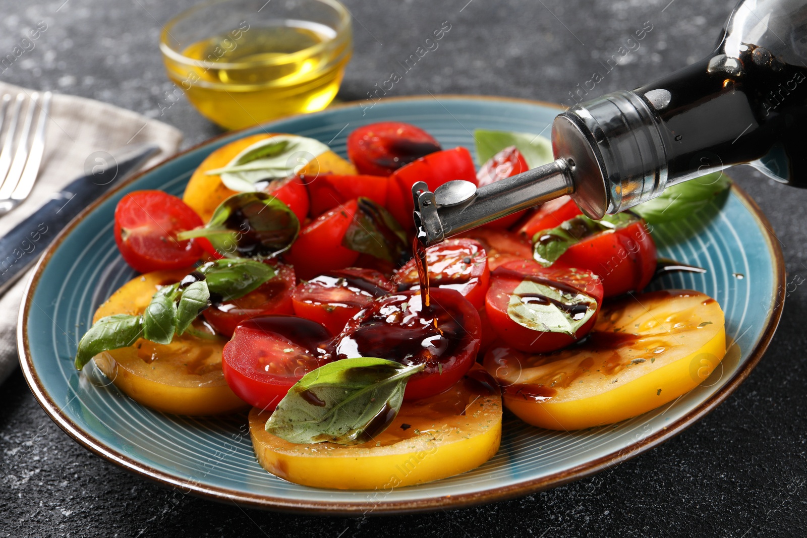 Photo of Pouring balsamic vinegar onto tasty salad on black textured table, closeup