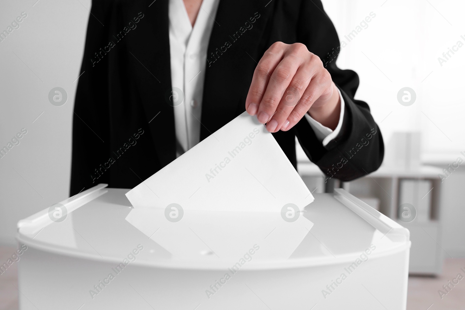 Photo of Woman putting her vote into ballot box indoors, closeup