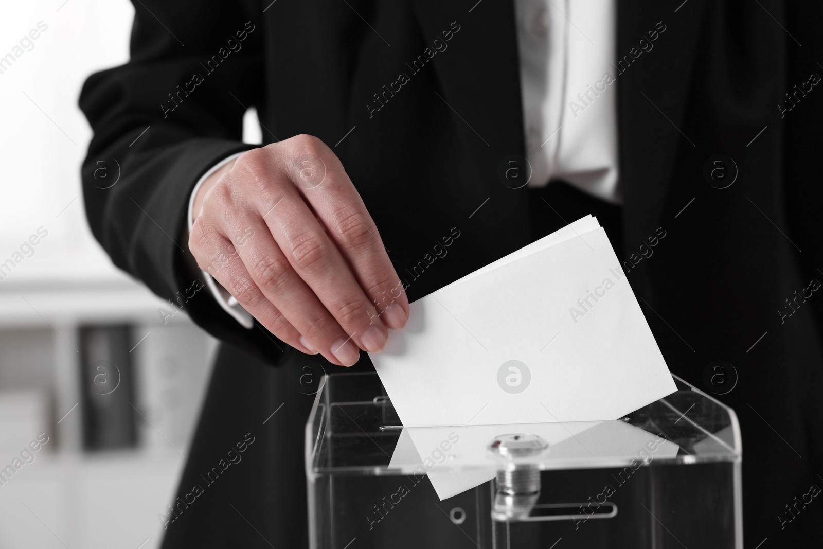 Photo of Woman putting her vote into ballot box indoors, closeup