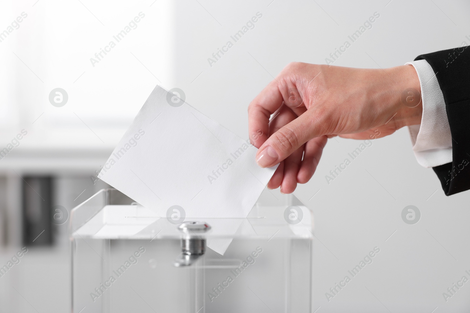 Photo of Woman putting her vote into ballot box indoors, closeup