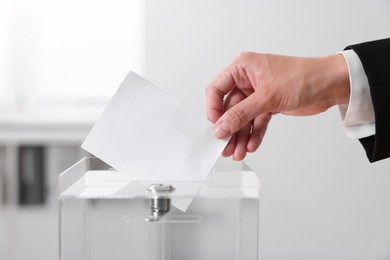 Photo of Woman putting her vote into ballot box indoors, closeup