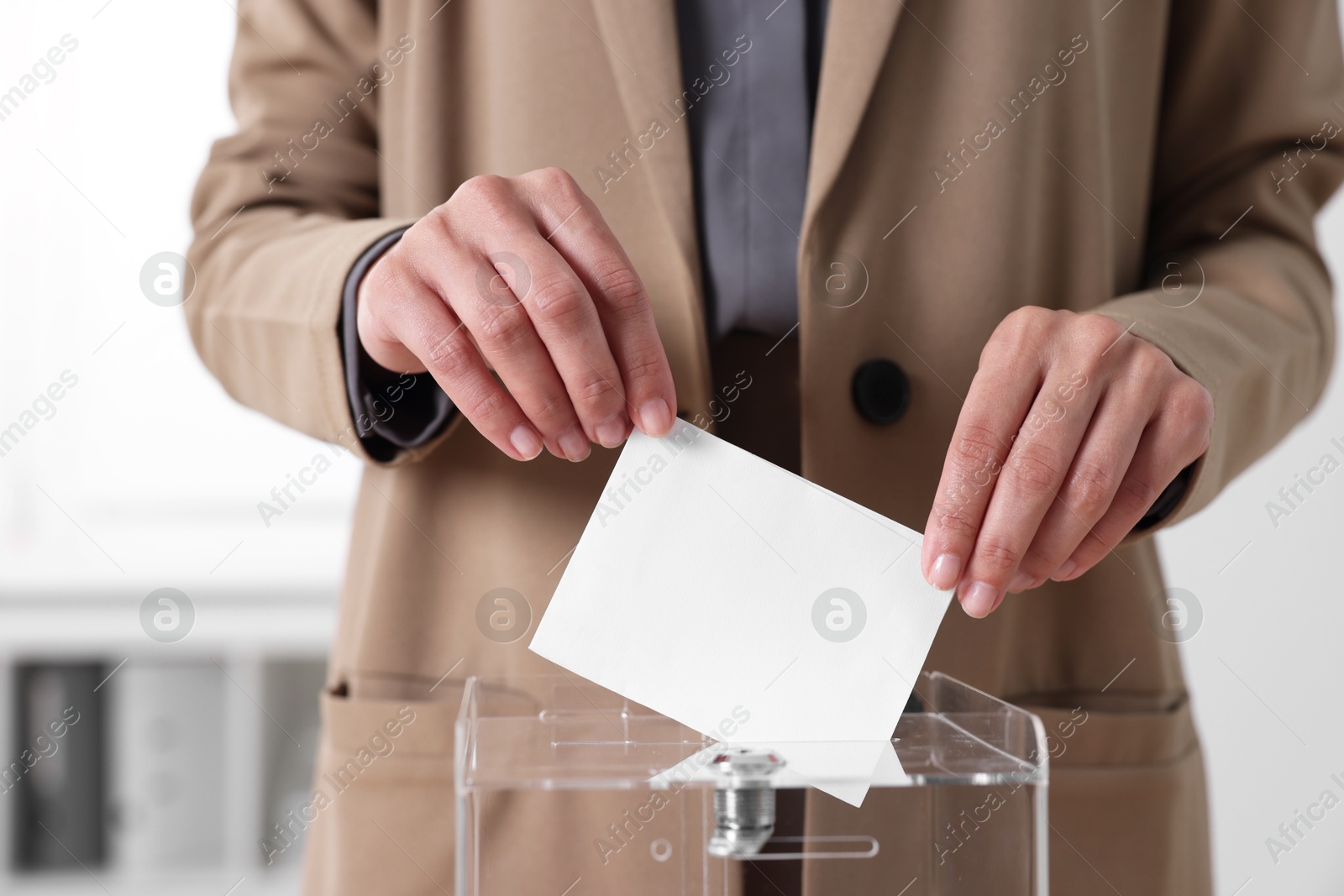 Photo of Woman putting her vote into ballot box indoors, closeup