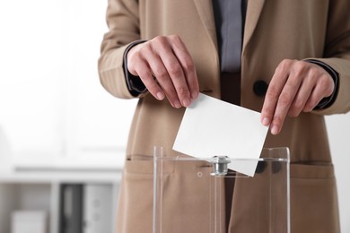 Photo of Woman putting her vote into ballot box indoors, closeup