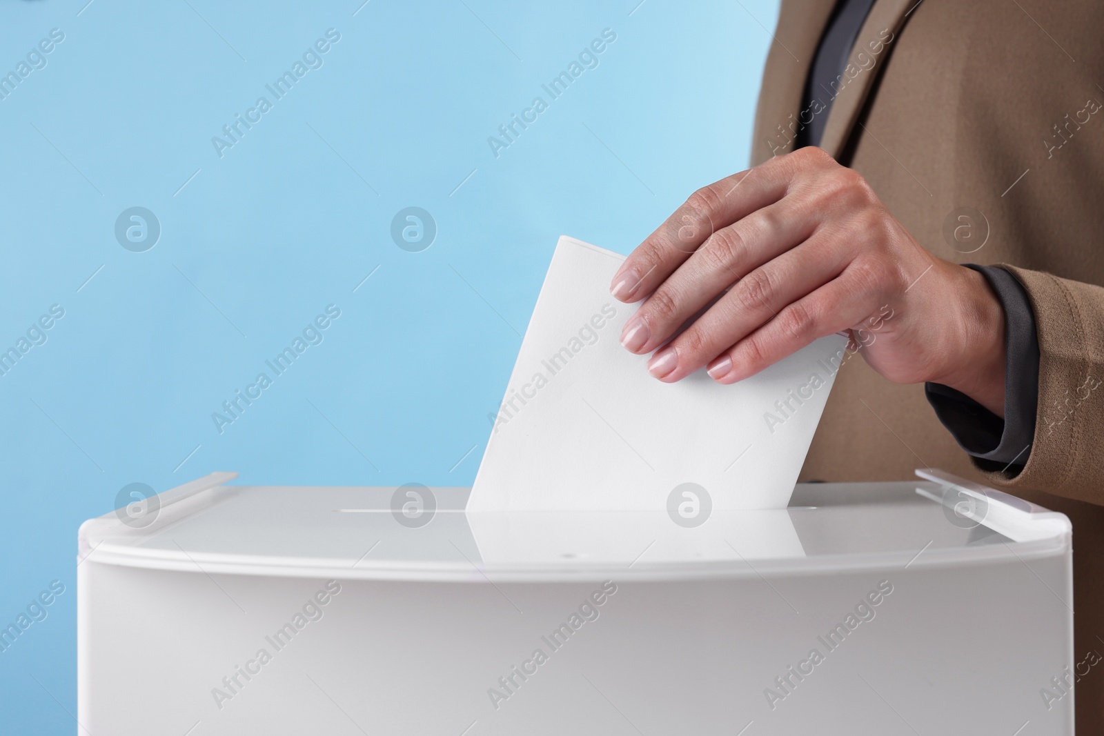 Photo of Woman putting her vote into ballot box against light blue background, closeup