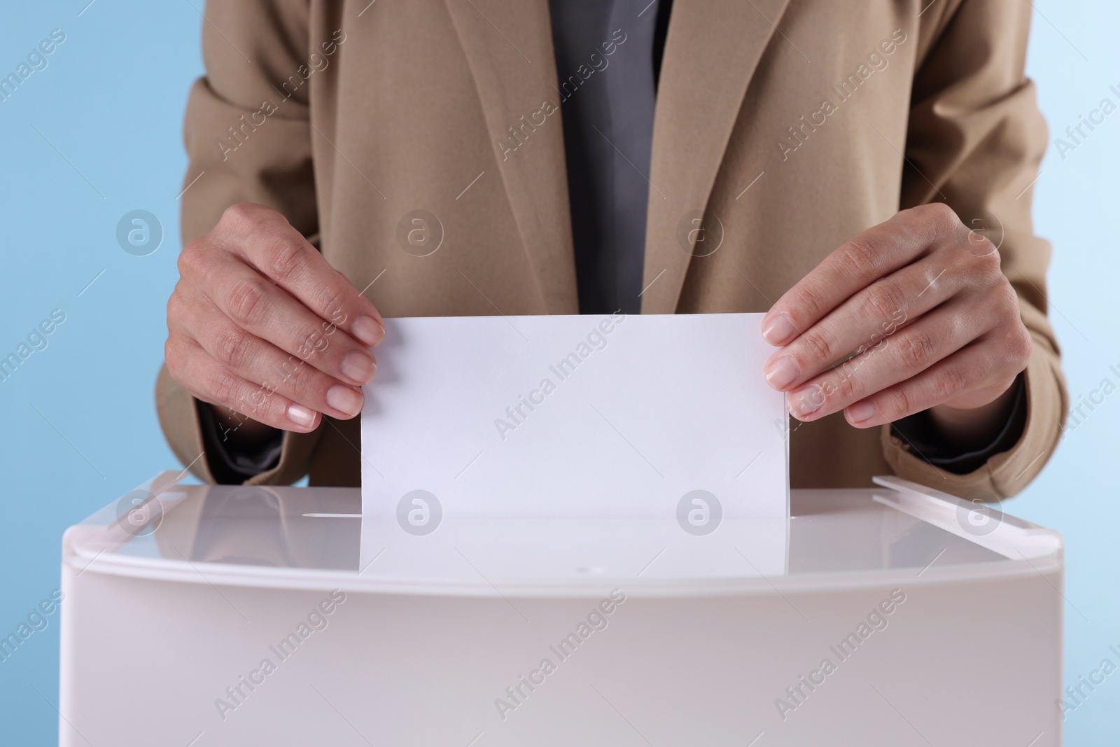 Photo of Woman putting her vote into ballot box against light blue background, closeup