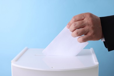 Photo of Man putting his vote into ballot box against light blue background, closeup