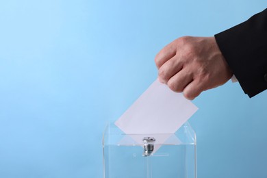 Man putting his vote into ballot box against light blue background, closeup. Space for text