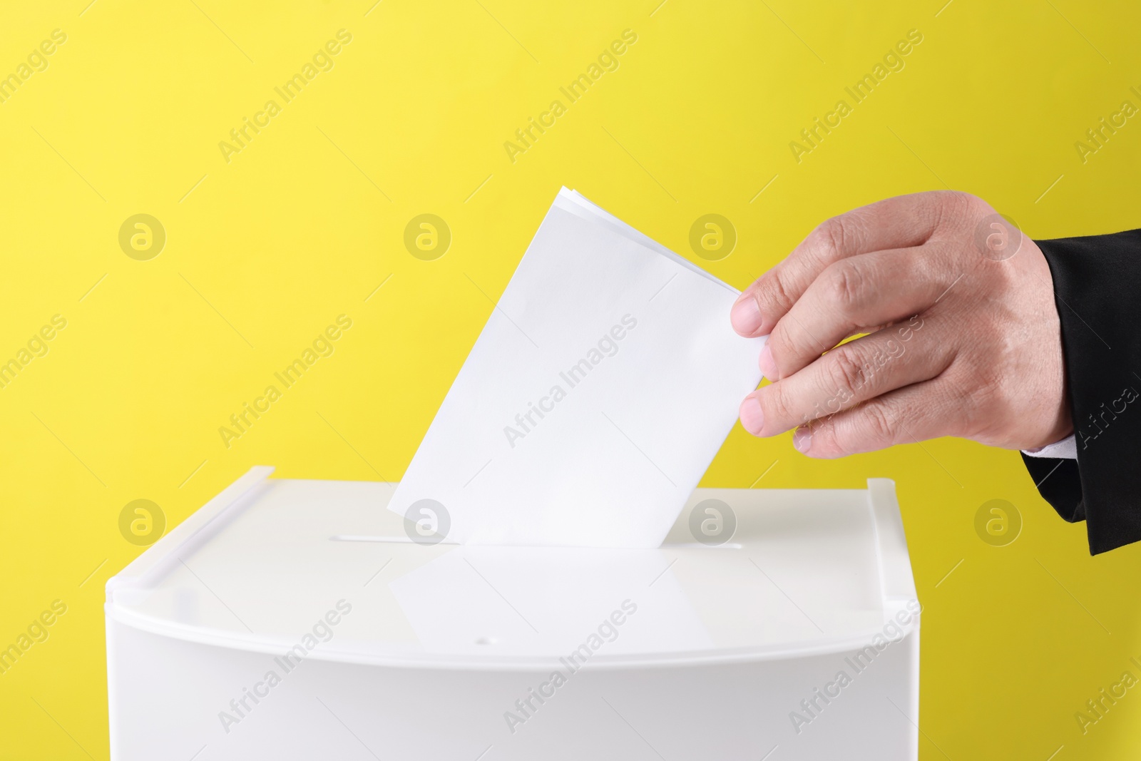 Photo of Man putting his vote into ballot box against yellow background, closeup