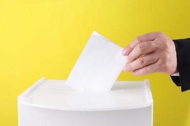 Man putting his vote into ballot box against yellow background, closeup