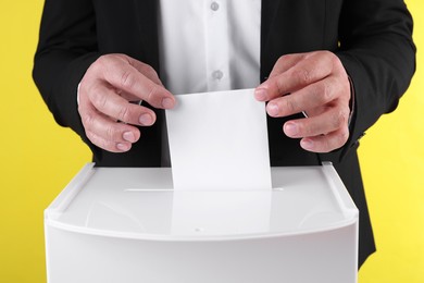 Man putting his vote into ballot box against yellow background, closeup