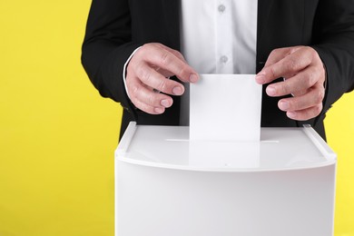 Photo of Man putting his vote into ballot box against yellow background, closeup