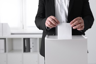 Man putting his vote into ballot box indoors, closeup. Space for text