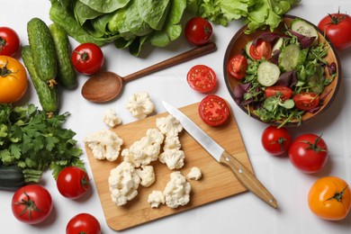 Photo of Healthy vegetarian food. Pieces of cauliflower, salad and vegetables on white tiled table, flat lay