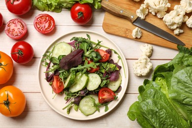 Photo of Healthy vegetarian food. Plate of salad and vegetables on light wooden table, flat lay