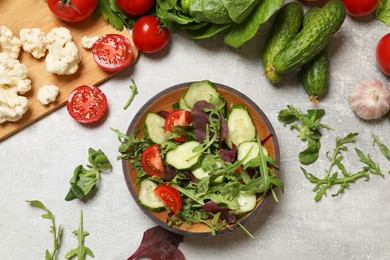 Photo of Healthy vegetarian food. Salad in bowl and vegetables on grey textured table, flat lay