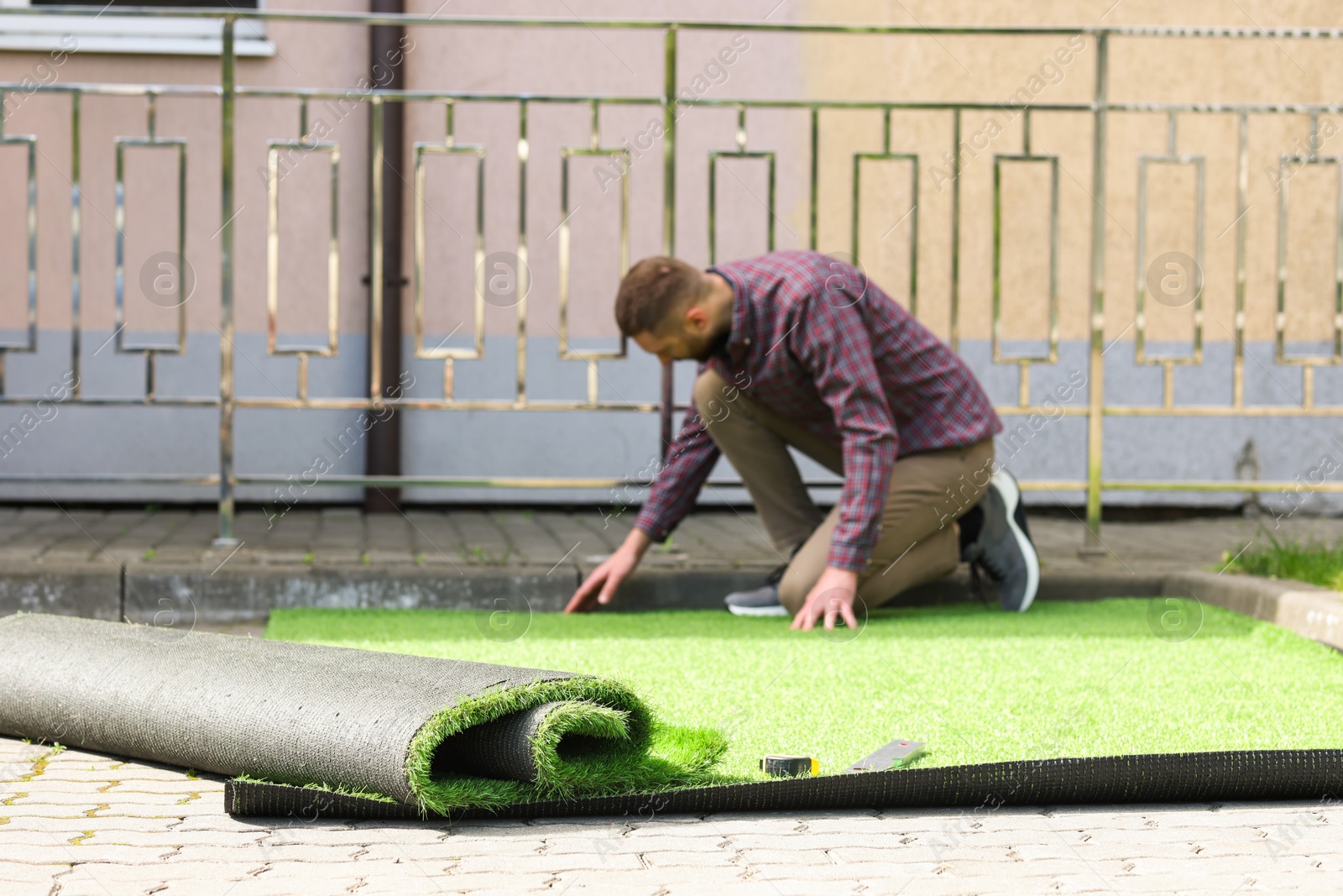 Photo of Young man installing artificial turf outdoors, selective focus