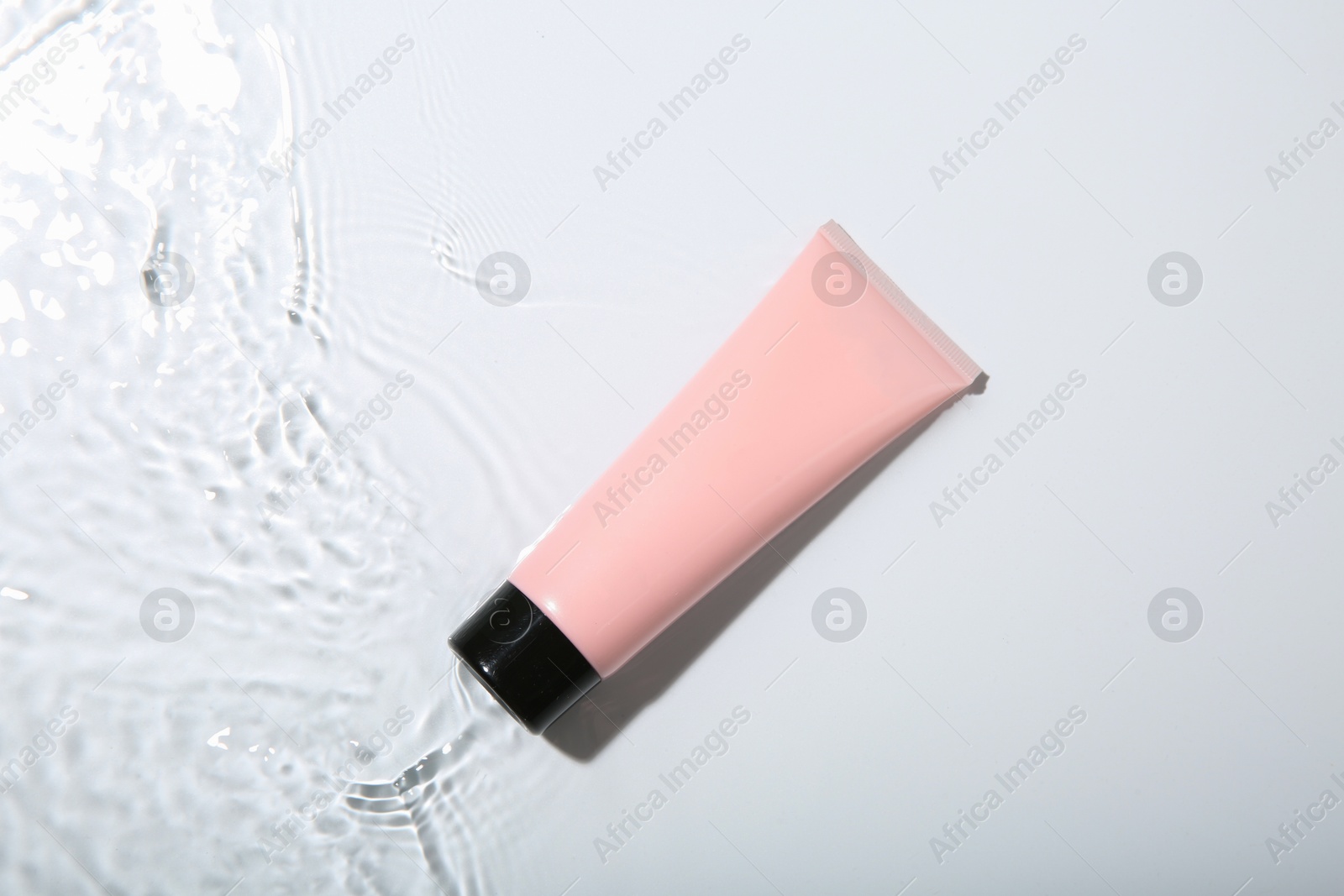 Photo of Cosmetic product. Tube with cream in water on light background, top view