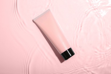 Photo of Cosmetic product. Tube with cream in water on light background, top view