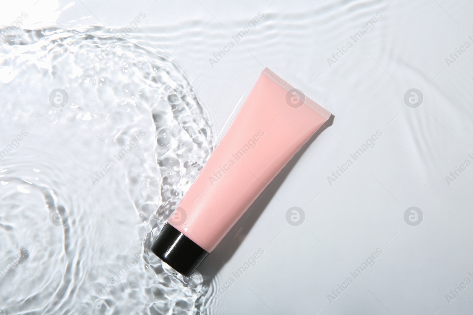 Photo of Cosmetic product. Tube with cream in water on light background, top view