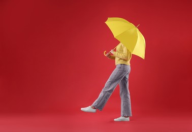 Woman with yellow umbrella walking on red background, space for text