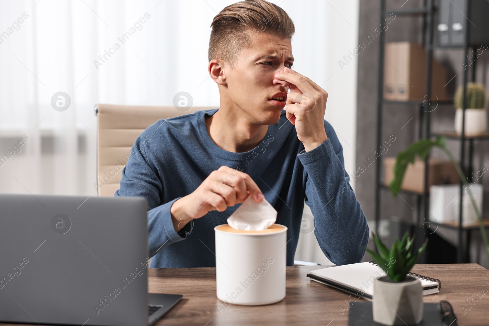 Photo of Young man with tissue suffering from sinusitis at wooden table indoors