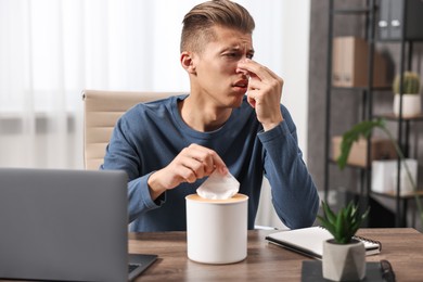 Photo of Young man with tissue suffering from sinusitis at wooden table indoors