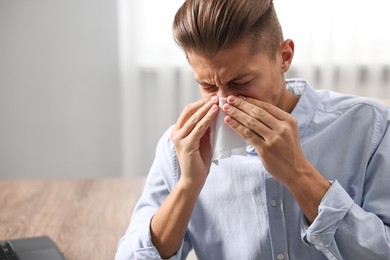 Photo of Young man with tissue suffering from sinusitis at wooden table indoors