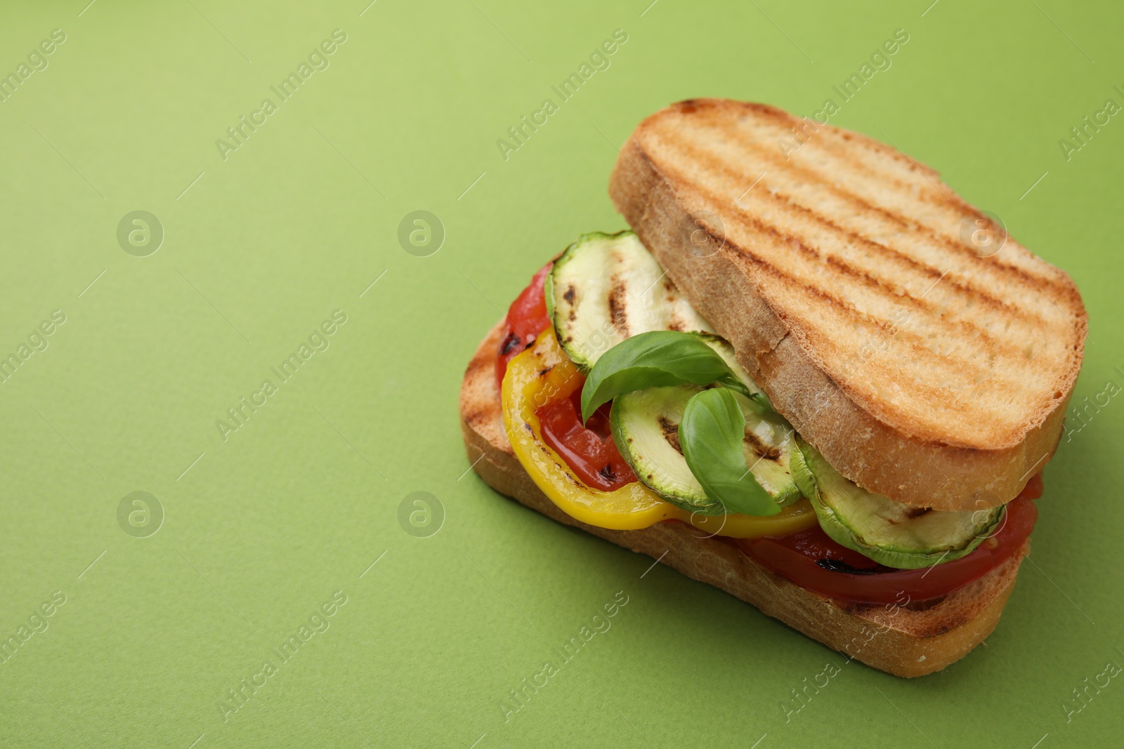 Photo of Tasty sandwich with grilled vegetables on green background, closeup. Space for text