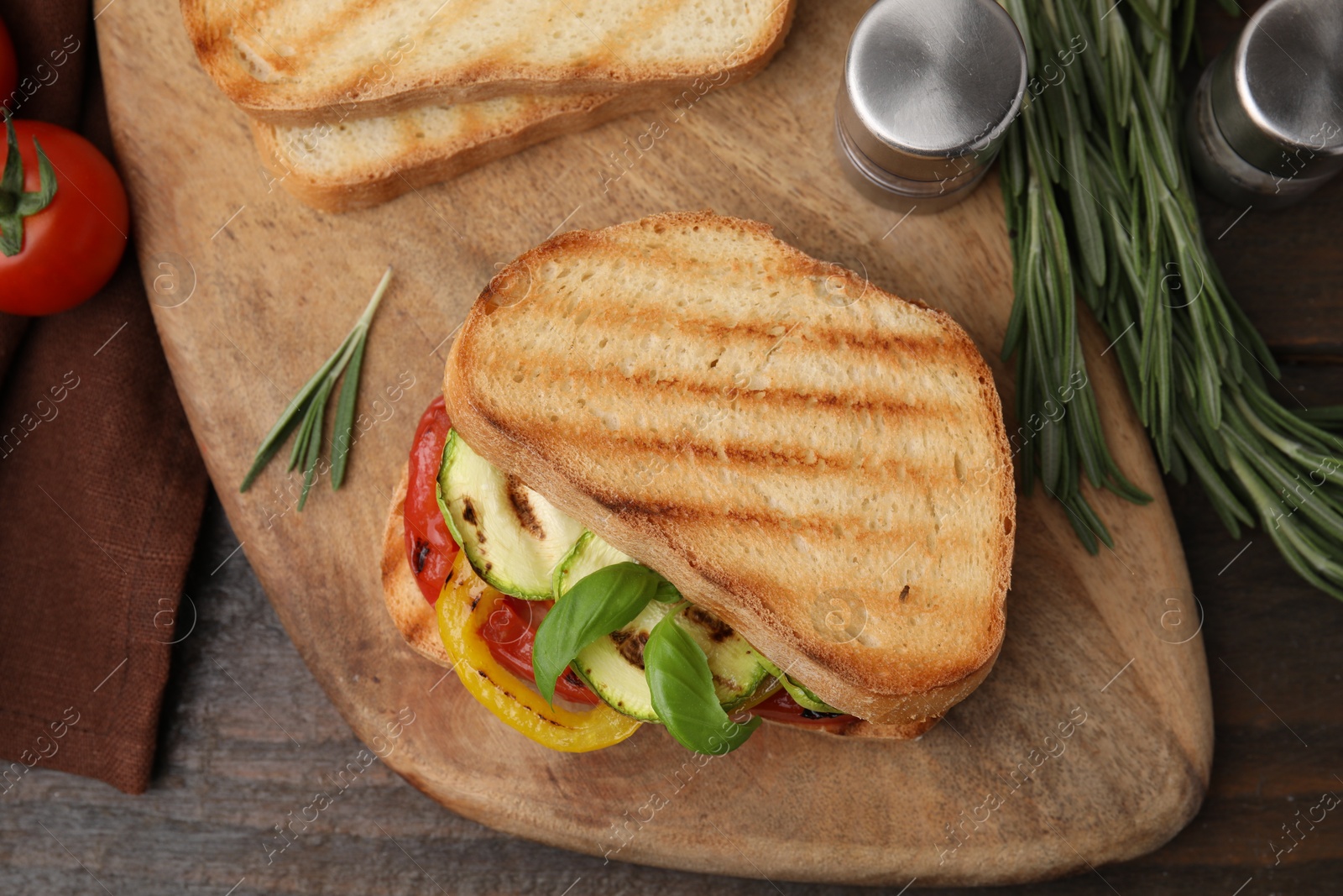 Photo of Tasty sandwich with grilled vegetables, rosemary and spices on wooden table, flat lay