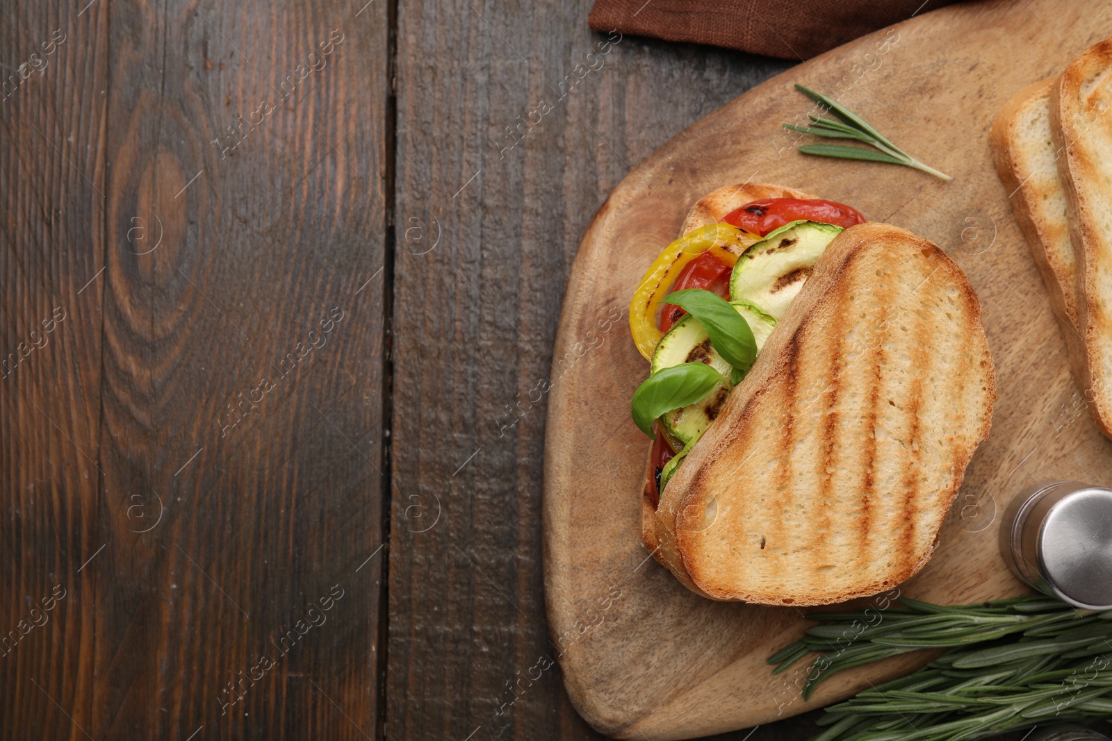 Photo of Tasty sandwich with grilled vegetables, rosemary and spices on wooden table, top view. Space for text