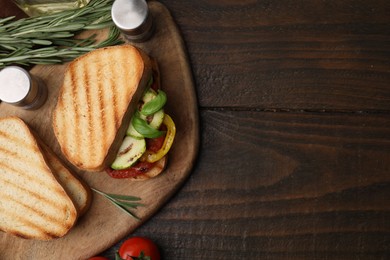 Tasty sandwich with grilled vegetables, rosemary and spices on wooden table, top view. Space for text