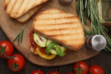 Photo of Tasty sandwich with grilled vegetables, rosemary, tomato and spices on wooden table, flat lay