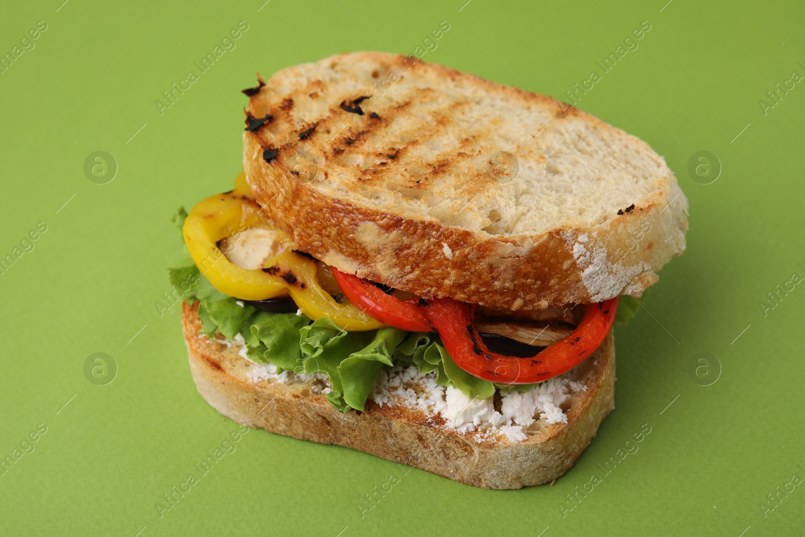 Photo of Tasty sandwich with grilled vegetables and cream cheese on green background, closeup