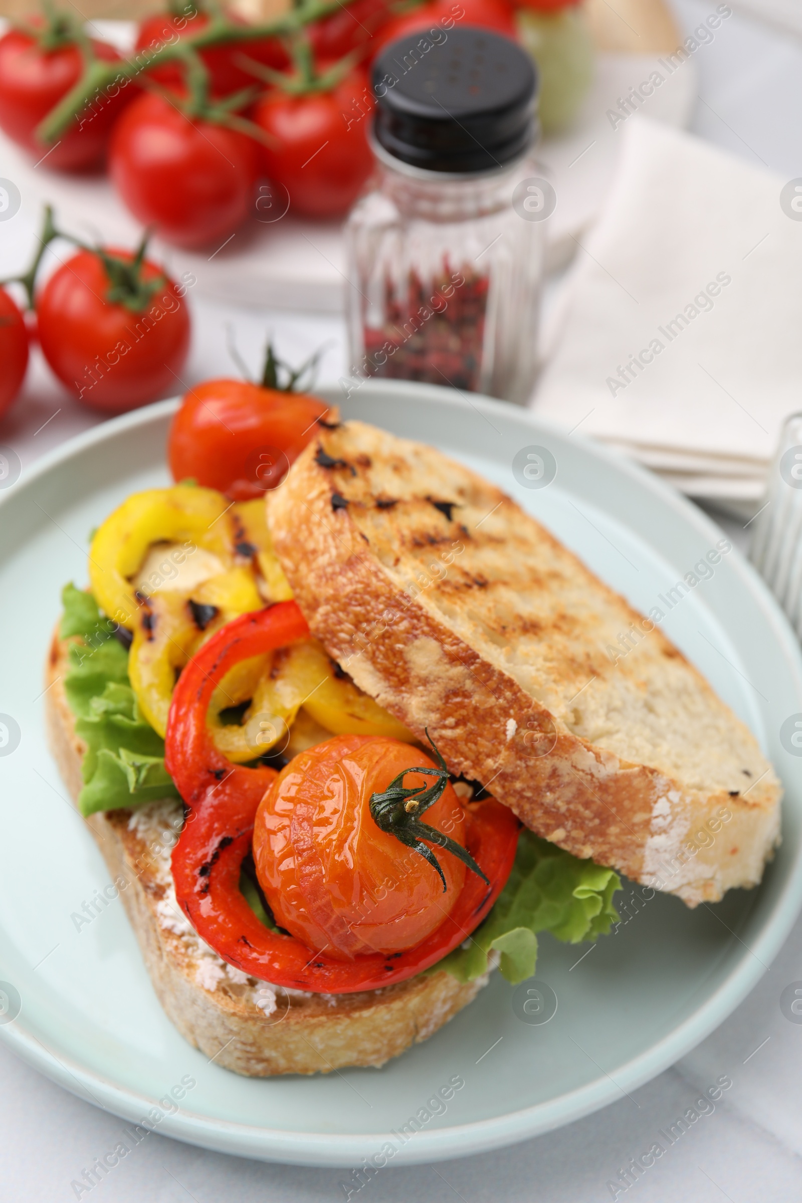 Photo of Tasty sandwich with grilled vegetables and cream cheese on white tiled table, closeup